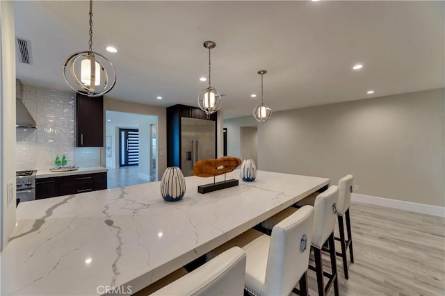 kitchen featuring light stone counters, decorative light fixtures, wall chimney exhaust hood, and appliances with stainless steel finishes