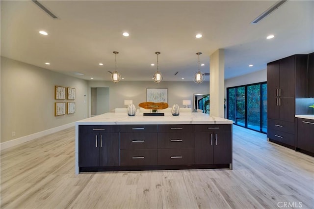 kitchen featuring hanging light fixtures, light stone countertops, dark brown cabinets, and light hardwood / wood-style flooring