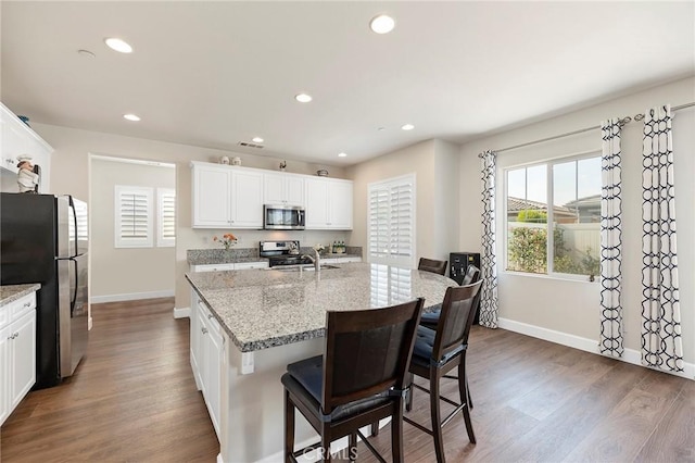 kitchen with light stone counters, stainless steel appliances, an island with sink, and white cabinets