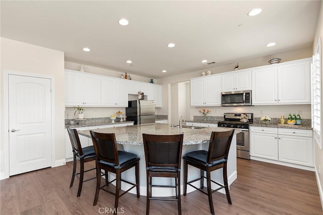 kitchen with stainless steel appliances, light stone countertops, a center island with sink, and white cabinets