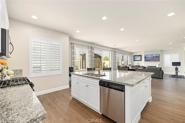 kitchen with stainless steel appliances, a kitchen island with sink, white cabinets, and light stone counters