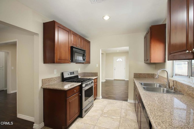 kitchen featuring light tile patterned flooring, stainless steel range with gas cooktop, light stone countertops, and sink