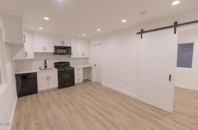 kitchen with sink, black appliances, white cabinets, a barn door, and backsplash