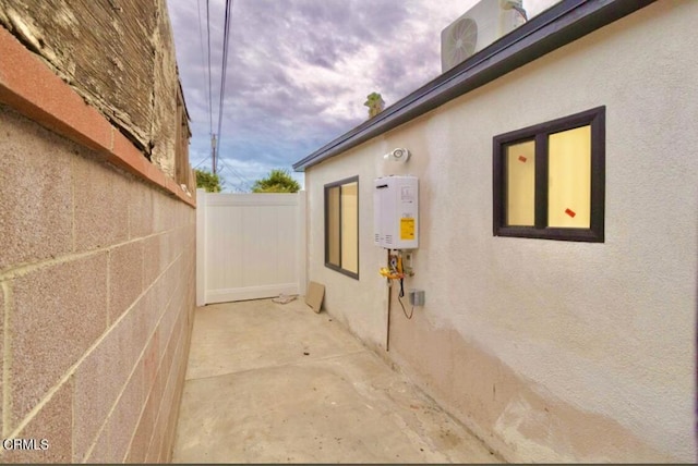 view of side of property with tankless water heater, a patio area, fence, and stucco siding