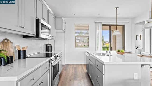 kitchen with sink, light stone counters, decorative light fixtures, an island with sink, and stainless steel appliances