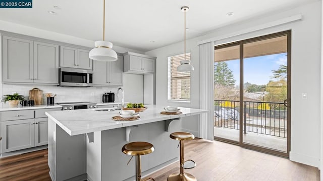 kitchen with light stone counters, sink, stainless steel appliances, and hanging light fixtures