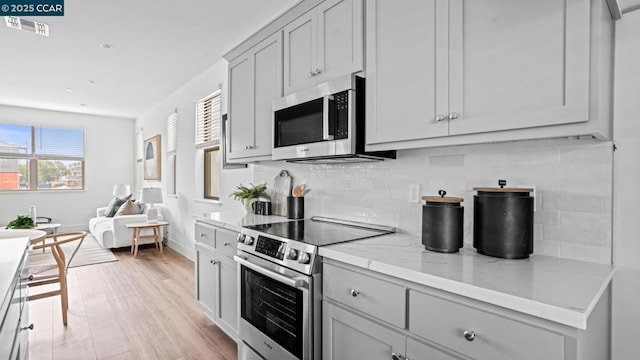 kitchen featuring light stone counters, light wood-type flooring, appliances with stainless steel finishes, gray cabinets, and decorative backsplash