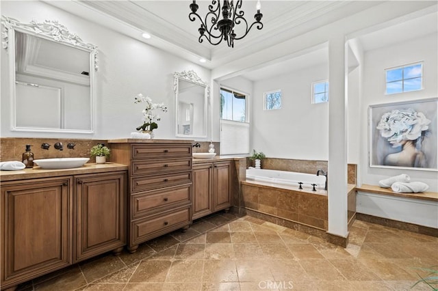 bathroom featuring a notable chandelier, ornamental molding, vanity, and tiled tub