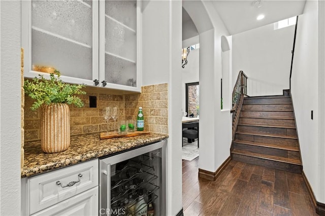 bar with backsplash, dark hardwood / wood-style floors, beverage cooler, white cabinets, and dark stone counters