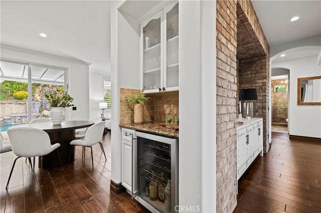 bar with dark wood-type flooring, backsplash, beverage cooler, white cabinets, and dark stone counters