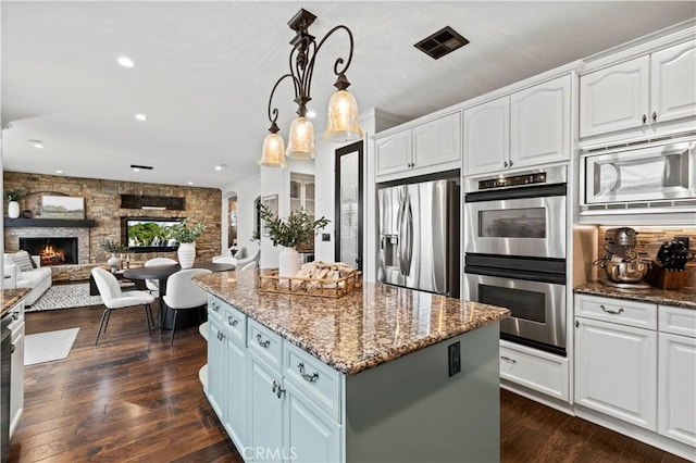 kitchen featuring white cabinetry, a fireplace, stainless steel appliances, and dark stone counters