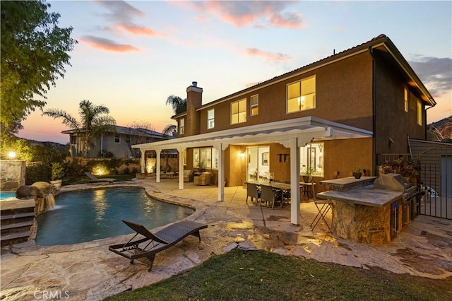 back house at dusk featuring a patio, a bar, an outdoor hangout area, pool water feature, and exterior kitchen