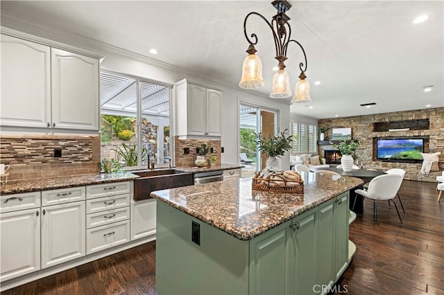 kitchen featuring hanging light fixtures, a stone fireplace, a center island, and white cabinets