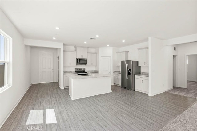 kitchen with white cabinetry, light hardwood / wood-style flooring, an island with sink, and appliances with stainless steel finishes