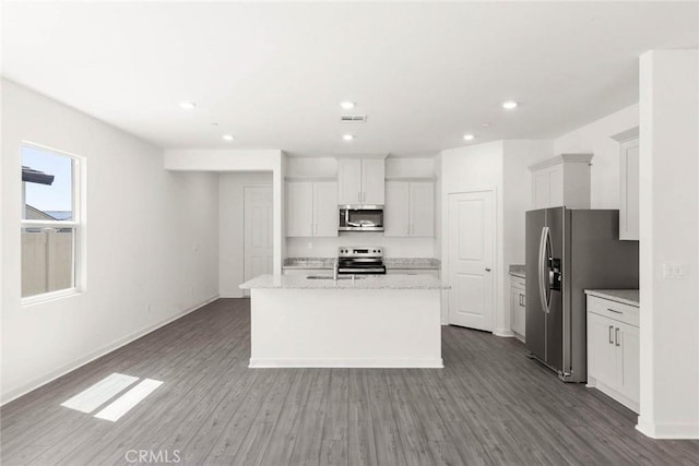 kitchen with appliances with stainless steel finishes, wood-type flooring, white cabinets, light stone counters, and a center island with sink