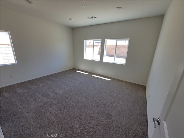 spare room featuring visible vents and dark colored carpet