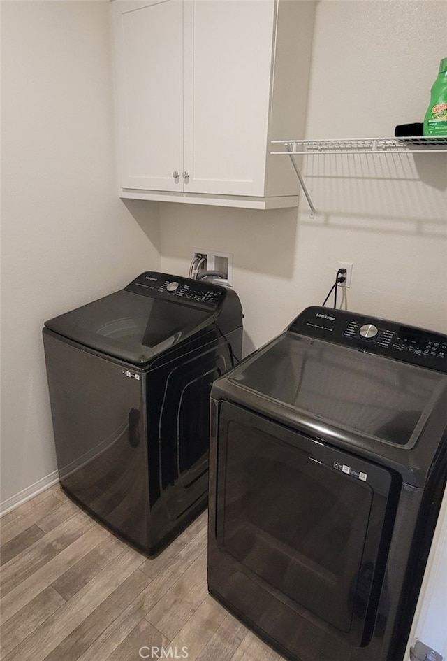 washroom with light wood-type flooring, cabinet space, baseboards, and separate washer and dryer