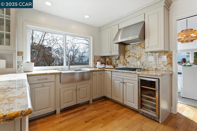 kitchen with stainless steel gas stovetop, backsplash, beverage cooler, light hardwood / wood-style floors, and wall chimney exhaust hood