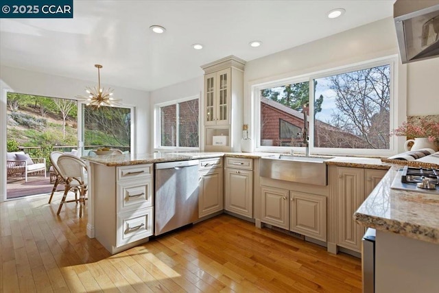 kitchen with decorative light fixtures, appliances with stainless steel finishes, light stone countertops, light hardwood / wood-style floors, and cream cabinetry