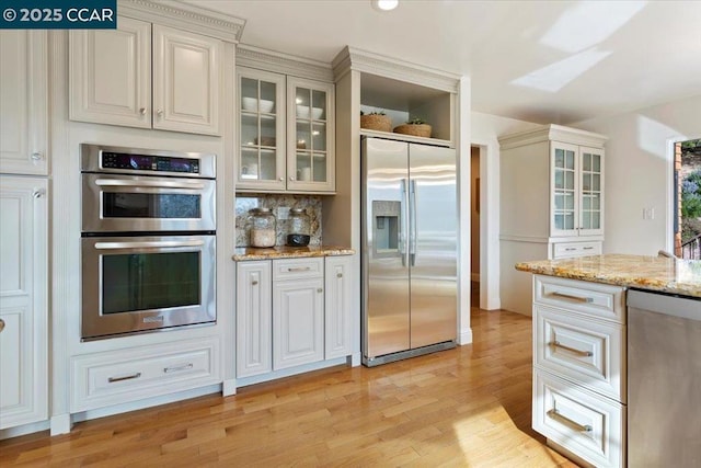 kitchen with light stone counters, light hardwood / wood-style flooring, stainless steel appliances, decorative backsplash, and white cabinets