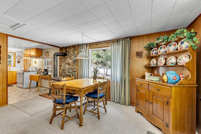 dining space with light carpet, wood walls, and a wood stove