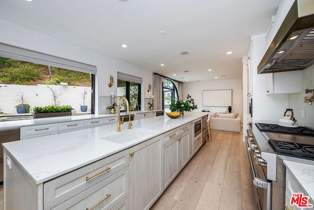 kitchen featuring wall chimney exhaust hood, sink, light stone counters, appliances with stainless steel finishes, and a kitchen island