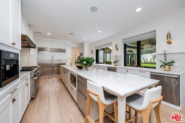 kitchen featuring white cabinetry, a spacious island, built in appliances, and light stone counters