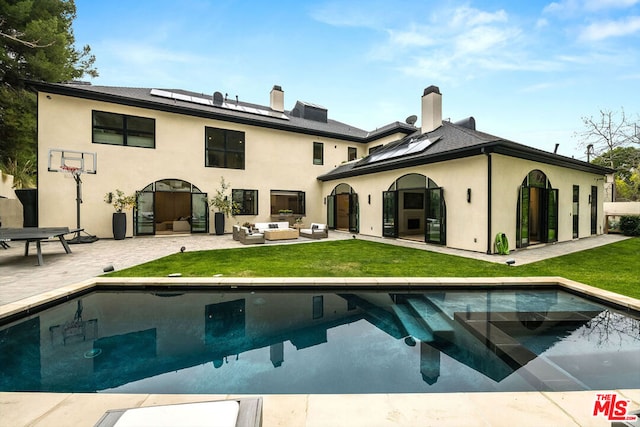 rear view of house featuring an outdoor living space, a lawn, a patio area, and solar panels