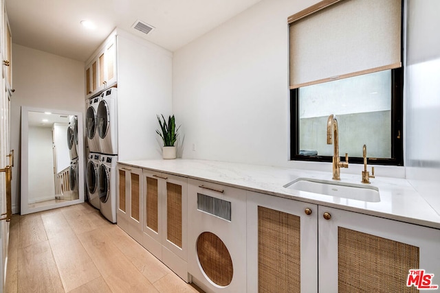 laundry room featuring cabinets, stacked washer and dryer, sink, and light wood-type flooring