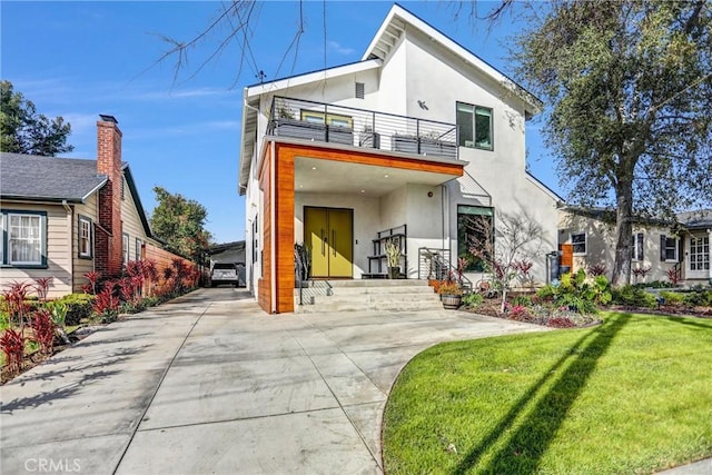 back of property featuring a balcony and a lawn