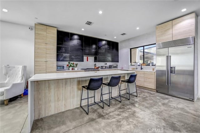 kitchen with a kitchen island, light brown cabinetry, a kitchen bar, decorative backsplash, and stainless steel built in fridge