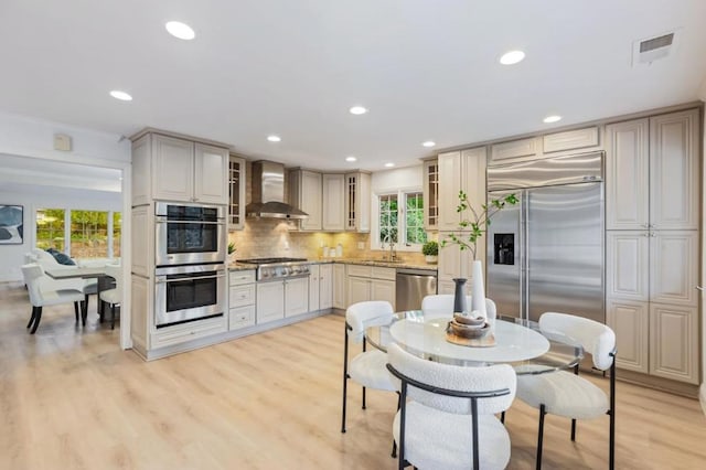 kitchen featuring sink, decorative backsplash, light hardwood / wood-style floors, stainless steel appliances, and wall chimney range hood