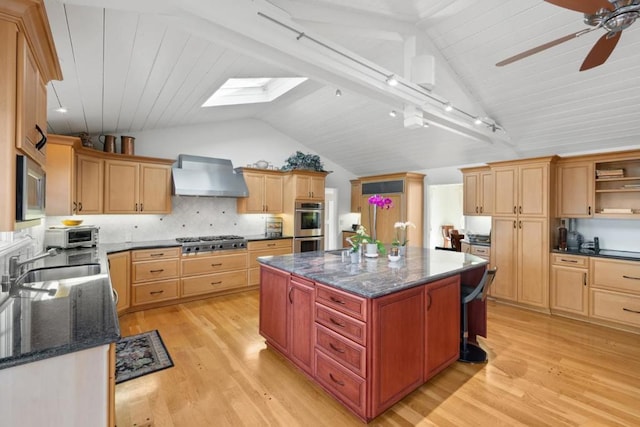 kitchen featuring appliances with stainless steel finishes, vaulted ceiling with skylight, a kitchen island, wall chimney exhaust hood, and light wood-type flooring