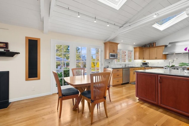 kitchen with decorative backsplash, light hardwood / wood-style flooring, vaulted ceiling with skylight, and appliances with stainless steel finishes