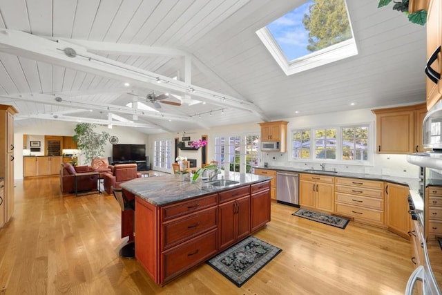 kitchen with appliances with stainless steel finishes, lofted ceiling with skylight, sink, and a center island with sink