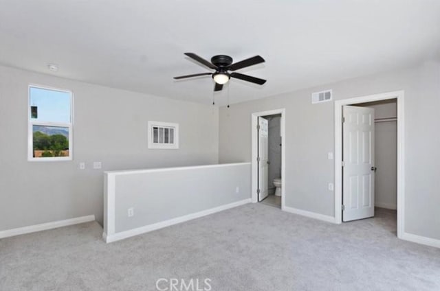 unfurnished bedroom featuring light carpet, a walk in closet, ceiling fan, and ensuite bathroom