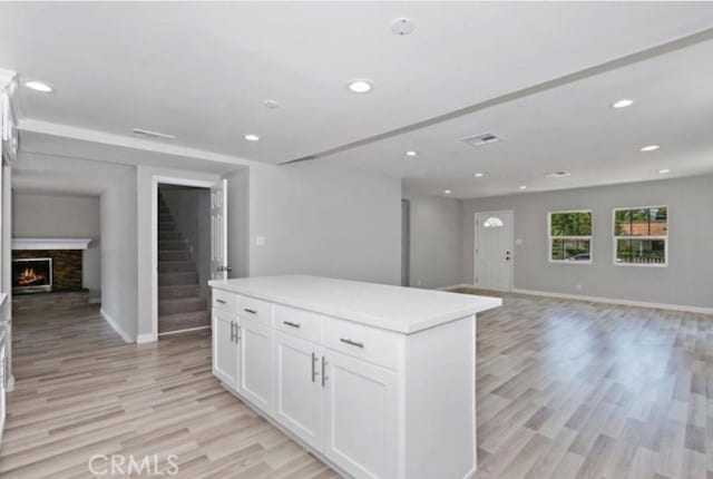 kitchen with light hardwood / wood-style flooring, a fireplace, white cabinets, and a kitchen island