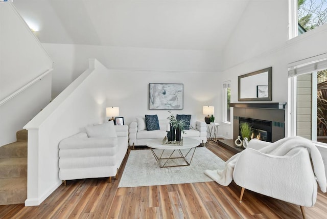 living room with a tiled fireplace, hardwood / wood-style floors, and high vaulted ceiling