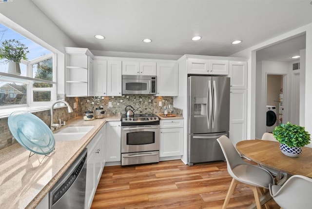 kitchen featuring sink, white cabinetry, stainless steel appliances, washer / dryer, and light wood-type flooring