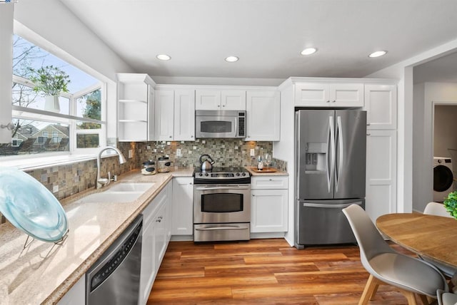 kitchen with washer / dryer, sink, light stone counters, stainless steel appliances, and white cabinets