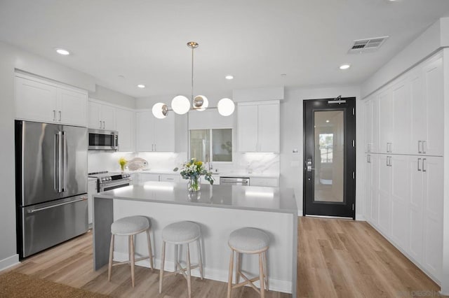 kitchen with appliances with stainless steel finishes, a center island, white cabinets, decorative light fixtures, and light wood-type flooring