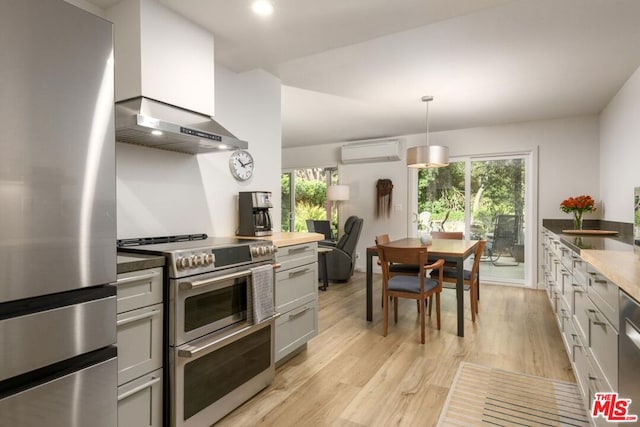 kitchen featuring appliances with stainless steel finishes, ventilation hood, hanging light fixtures, a wall unit AC, and light hardwood / wood-style flooring