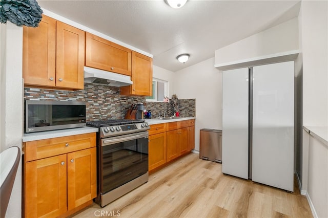 kitchen with tasteful backsplash, appliances with stainless steel finishes, sink, and light wood-type flooring