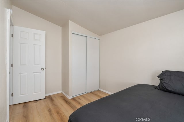 bedroom featuring vaulted ceiling, light wood-type flooring, and a closet