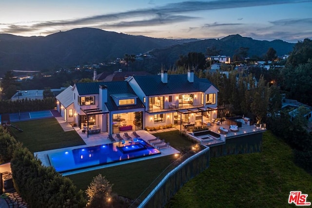 back house at dusk featuring a patio, a balcony, a yard, an outdoor hangout area, and a mountain view