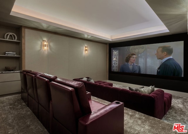 carpeted cinema room with built in shelves and a raised ceiling