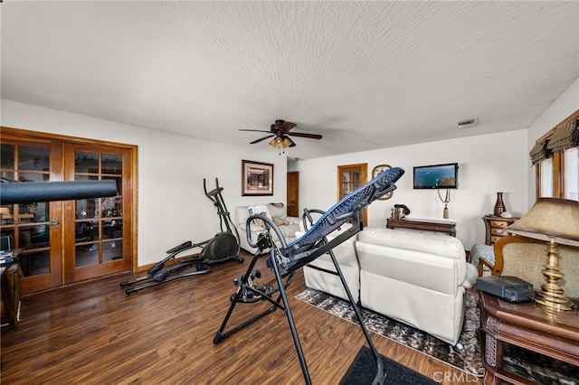 workout area with ceiling fan, dark wood-type flooring, and a textured ceiling