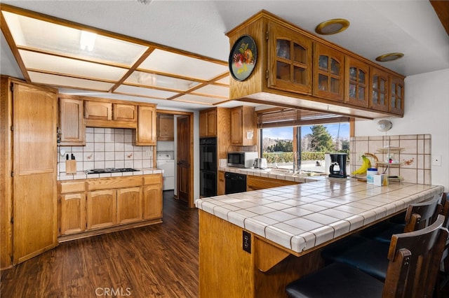 kitchen featuring tasteful backsplash, tile counters, black appliances, dark hardwood / wood-style flooring, and kitchen peninsula