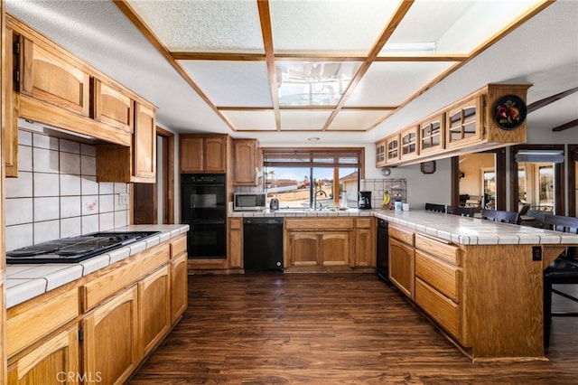 kitchen featuring black appliances, tile counters, a kitchen bar, and kitchen peninsula