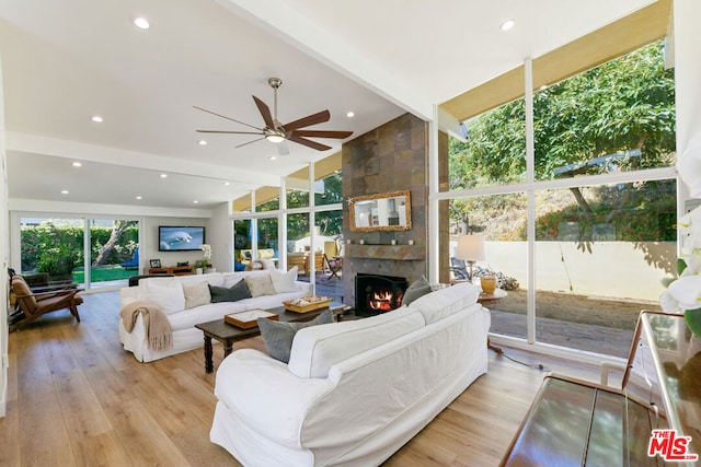 living room with light hardwood / wood-style flooring, a wall of windows, a large fireplace, and beamed ceiling